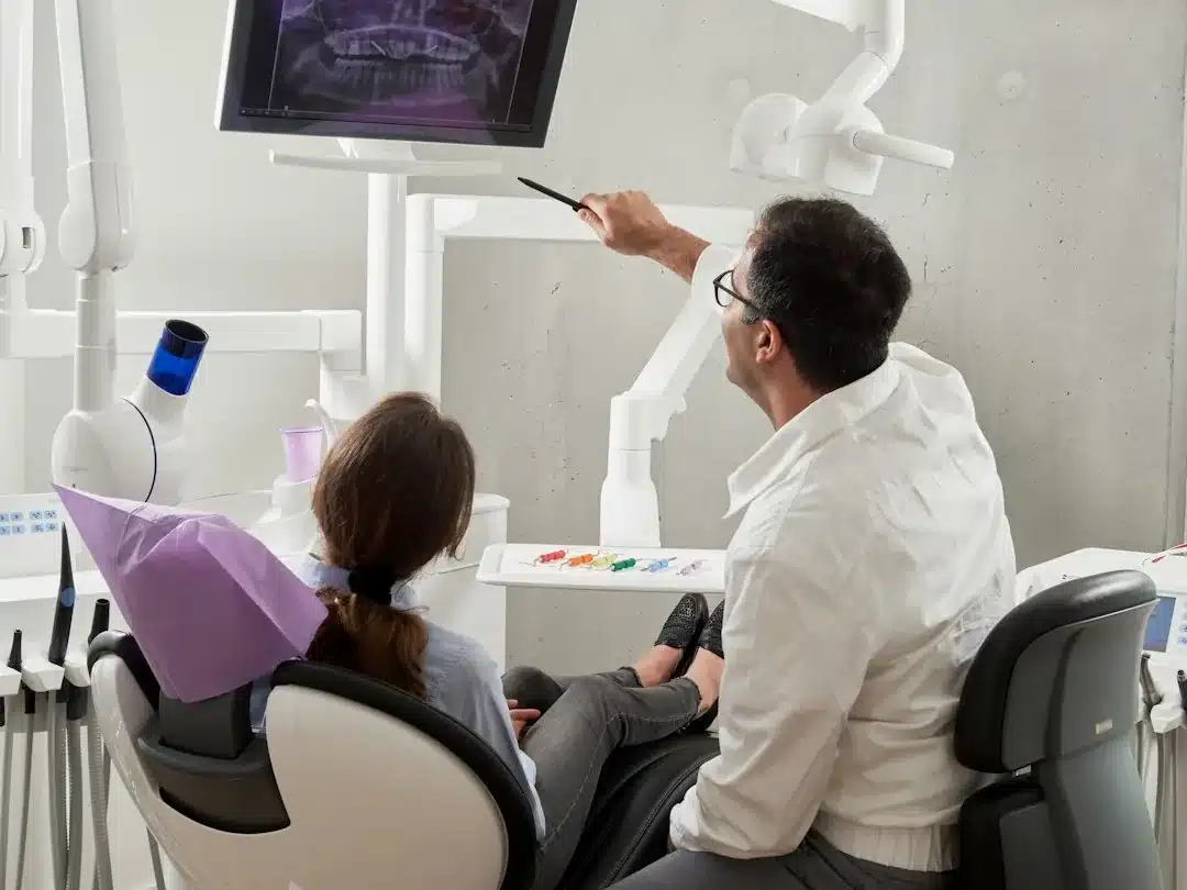 Dentiste pointant une radiographie dentaire sur écran devant une patiente en fauteuil