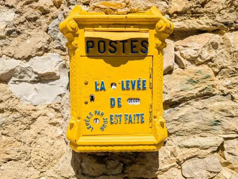Boîte aux lettres jaune ancienne en fonte avec inscription POSTES sur mur de pierre